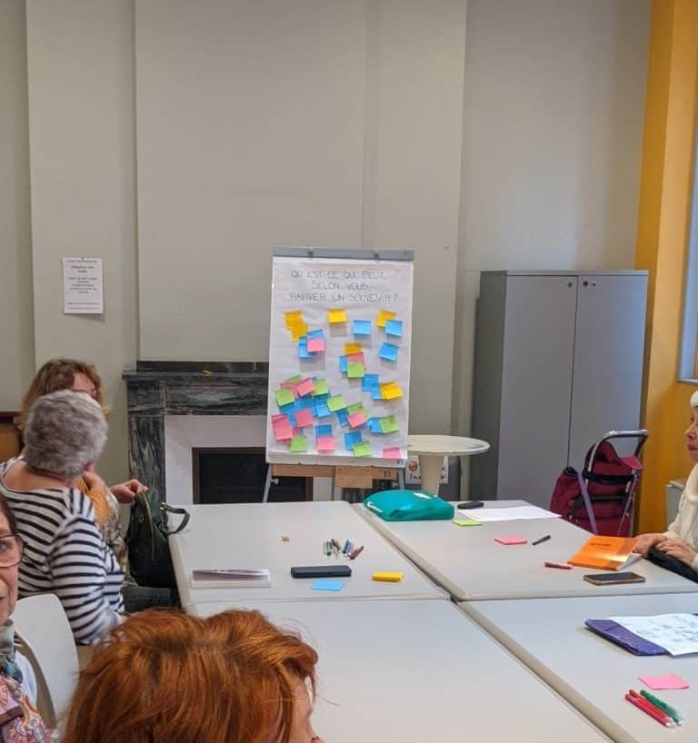 Des personnes autour d’une grande table participent à l’atelier. Un tableau est rempli de post-it.