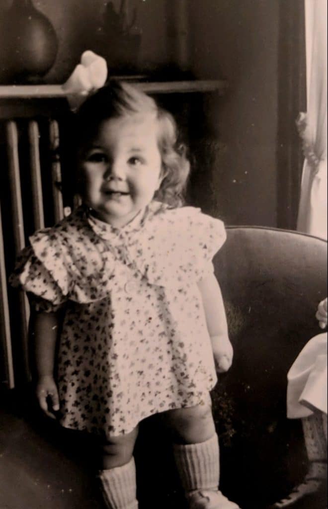 Paule à 2 ans dans une petite robe à fleur. Elle regarde l'objectif en souriant.